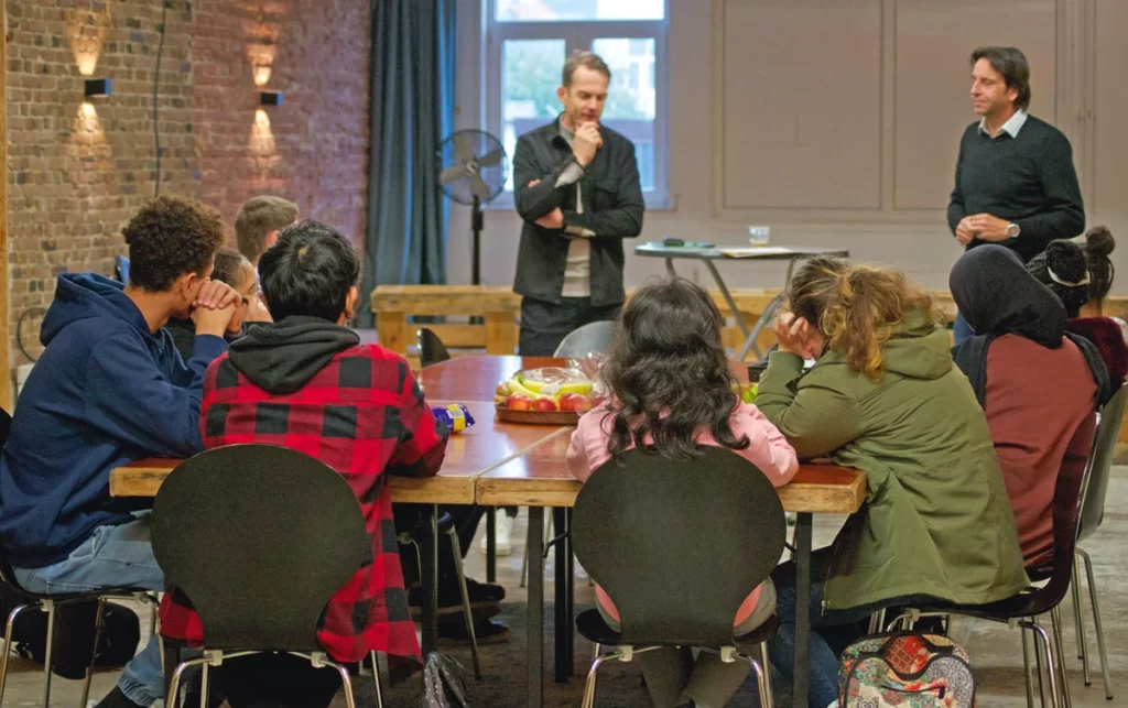 Een man die voor een groep mensen staat die aan een tafel zitten